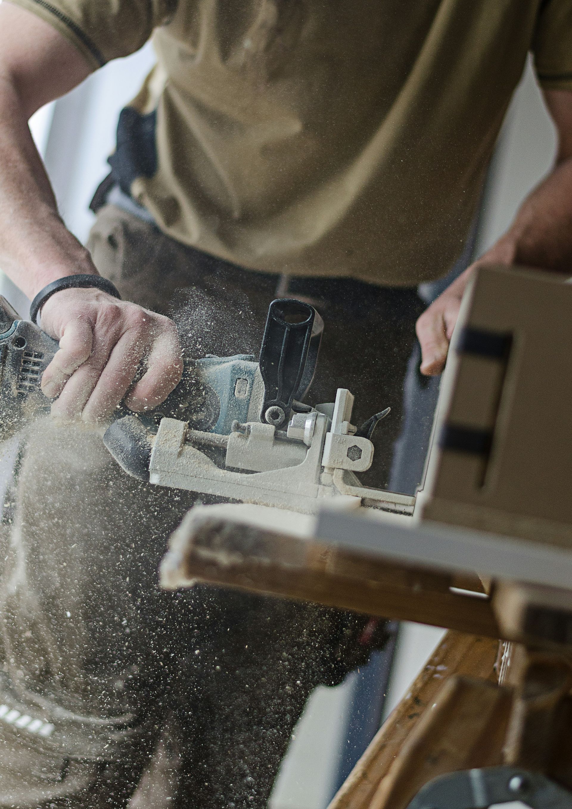 A person using a biscuit joiner to cut a slot in a wooden board